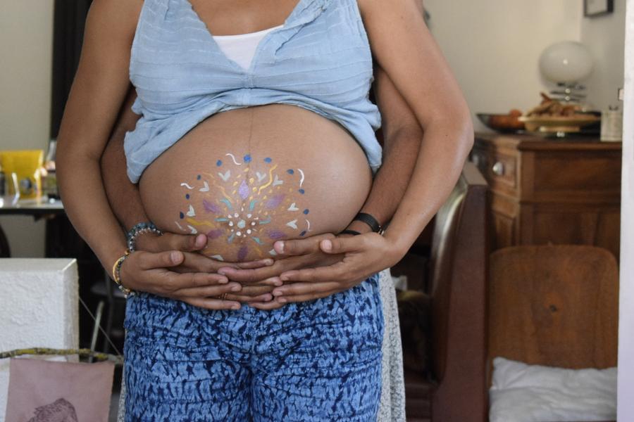 Ventre peint d'un mandala, soutenu par les mains de la future maman et de son conjoint