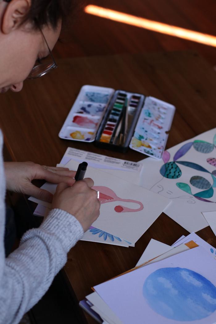 Andréa peint à l'aquarelle, entourée de ses couleurs et de feuilles déjà peintes