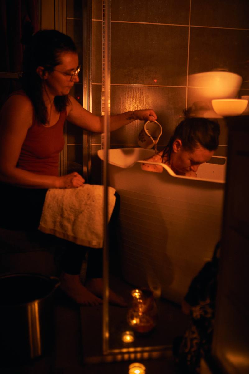 Andréa verse de l'eau à la coupelle sur la nuque d'une maman, à la lueur des bougies